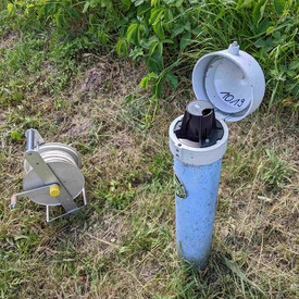Rohr einer Grundwassermesstelle, das ca. 0,5 m aus dem Boden ragt. 